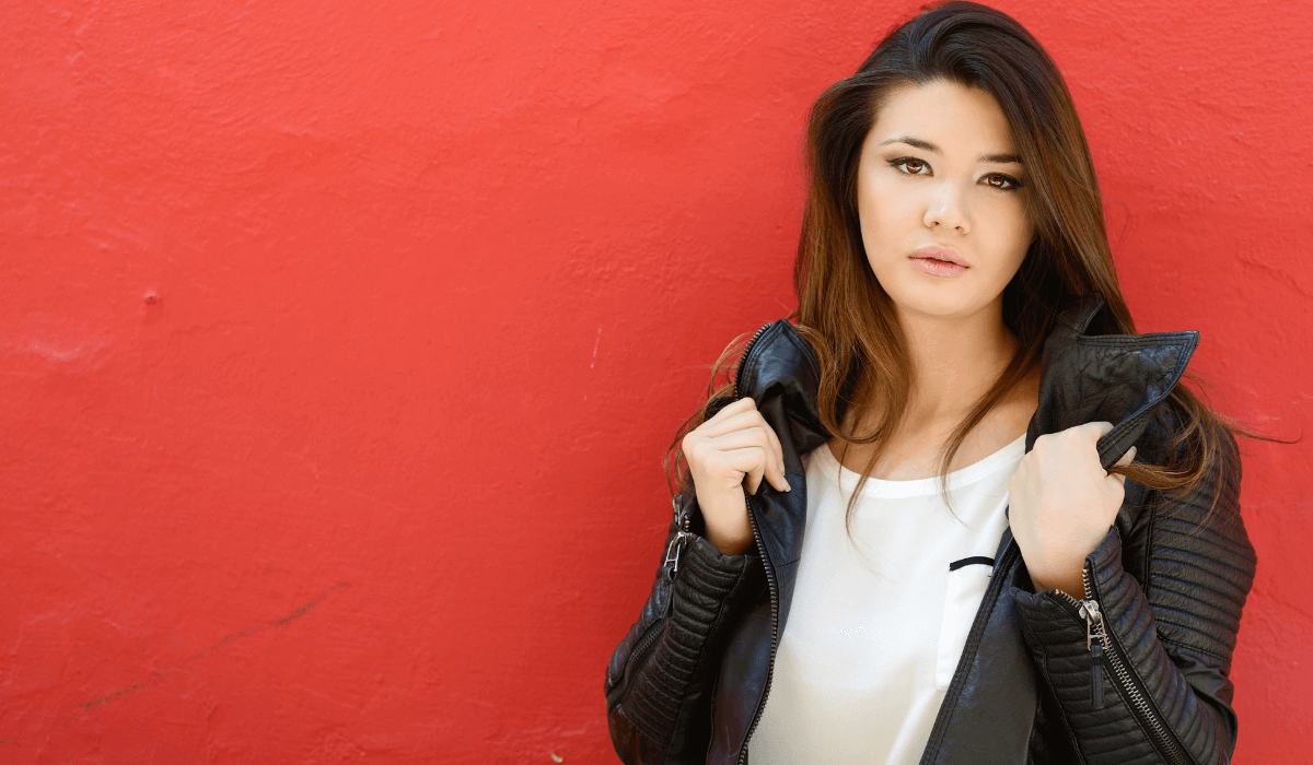 Woman wearing a beautiful leather jacket after caring for it with URAD leather conditioner. Standing with a red background.